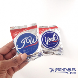 A hand holds two small, silver-wrapped candy packages, one with a blue sticker featuring "JOW" and "for eternity! Romans 8:38-39", and the other with a blue sticker featuring "York" and "Get the sensation!", both wrappers stating "As Always... 70% Less Fat!" and "140 calories".