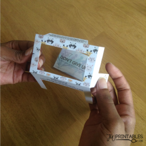 Hands hold a partially assembled paper craft frame with a cartoon animal pattern, revealing a small card inside that reads "2017 DON'T GIVE UP! CONVENTION OF JEHOVAH'S WITNESS".