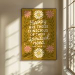 A framed poster with a mustard yellow background, floral designs, and the text "HAPPY ARE THOSE CONSCIOUS OF THEIR Spiritual need MATTHEW 5:3" hangs on a wall, illuminated by sunlight casting window shadows.