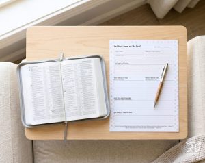 An open Bible showing text in multiple languages and a planner titled "Faithful Ones of the Past" with a pen are displayed on a light wooden tray.
