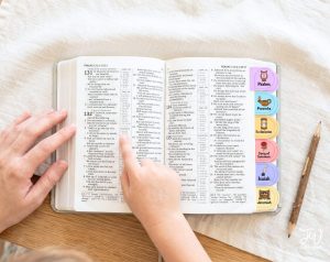A person's hands hold an open Bible displaying text from Psalms, with colorful book tabs for various books of the Bible, including Psalms, Proverbs, Ecclesiastes, Song of Solomon, Isaiah, and Jeremiah, next to a wooden pencil and a "JW printables" logo.