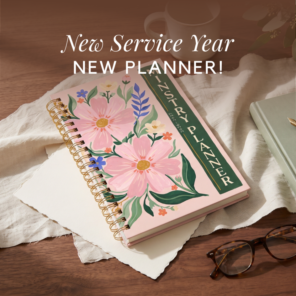 A pink floral planner with gold spiral binding, labeled "MINISTRY PLANNER 2026-2027", rests on white paper and a light cloth on a wooden table, with text overlay "New Service Year NEW PLANNER!".