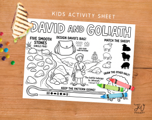 A kids' activity sheet titled "David and Goliath" is displayed on a wooden table with crayons, a sandwich, and candies, featuring various tasks like circling stones, designing a bag, matching sheep, and completing a pattern.